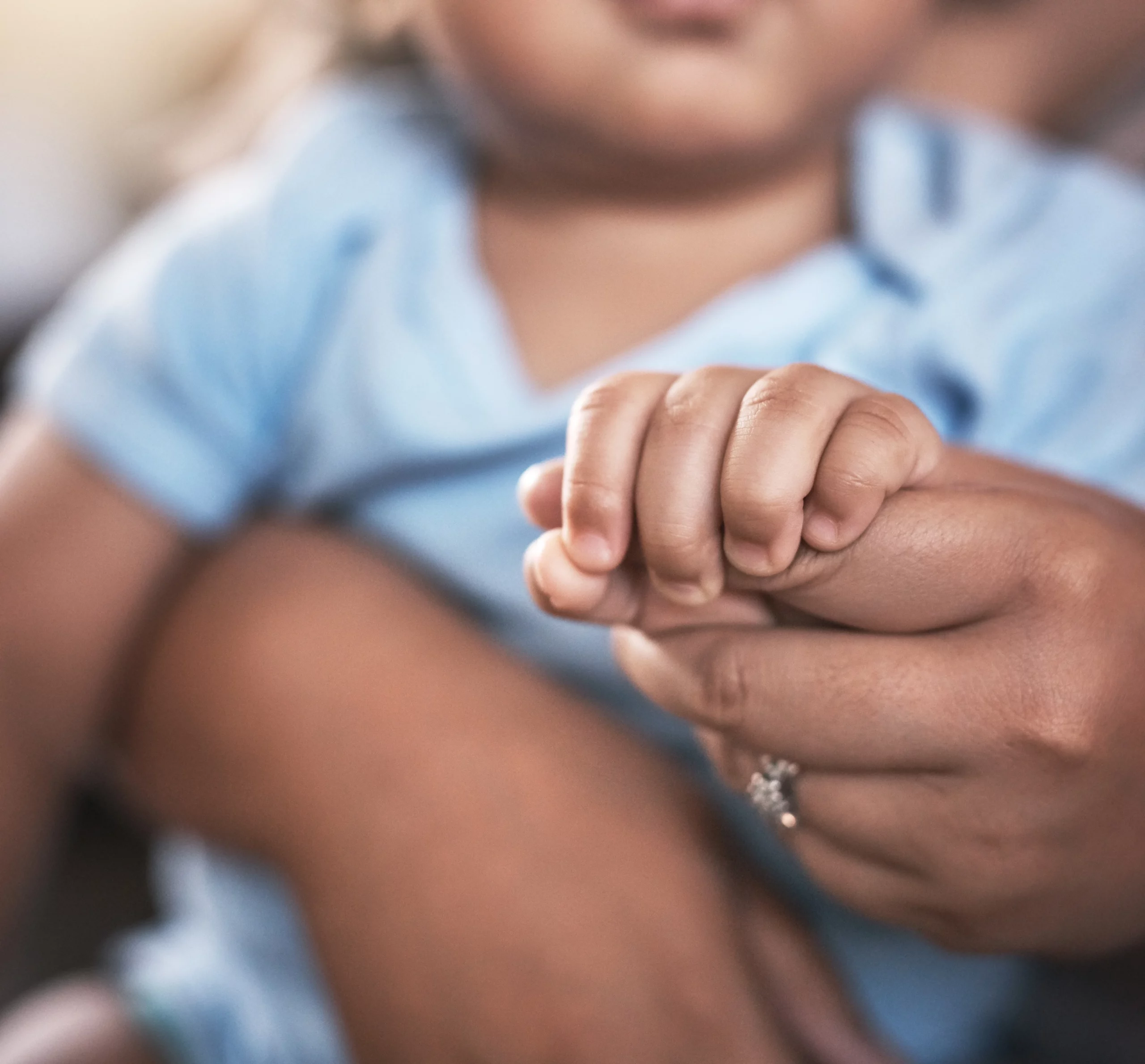 Baby in light blue shirt gently holds an adult’s finger, conveying warmth and connection—underscoring the importance of child support in Florida.