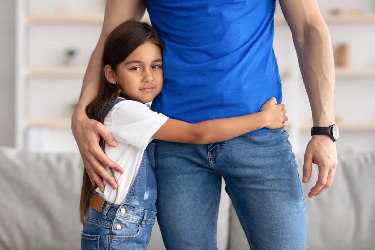 Young girl in denim overalls hugging an adult in a blue shirt in a cozy home, symbolizing warmth, security, and the importance of stable custody in Florida family law.